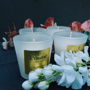 A rose-scented candle sits atop a table with two cups of drinkware, surrounded by a bouquet of fresh flowers.